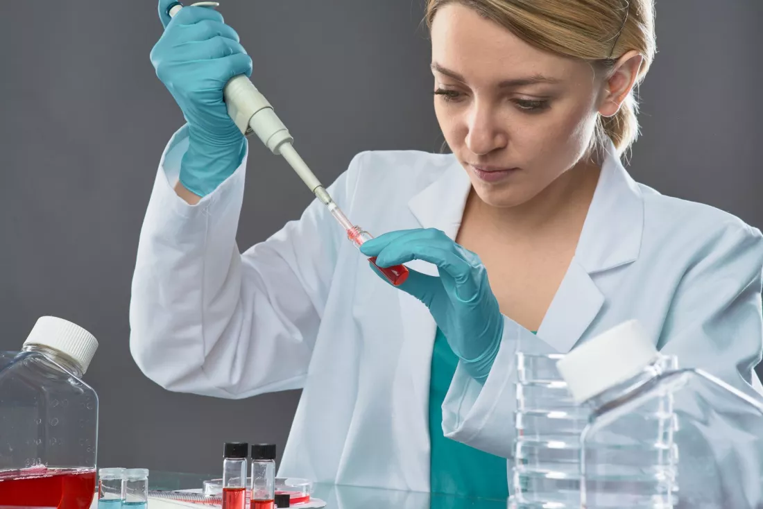Młoda laborantka w rękawiczkach odmierza pipetą próbkę w laboratorium.