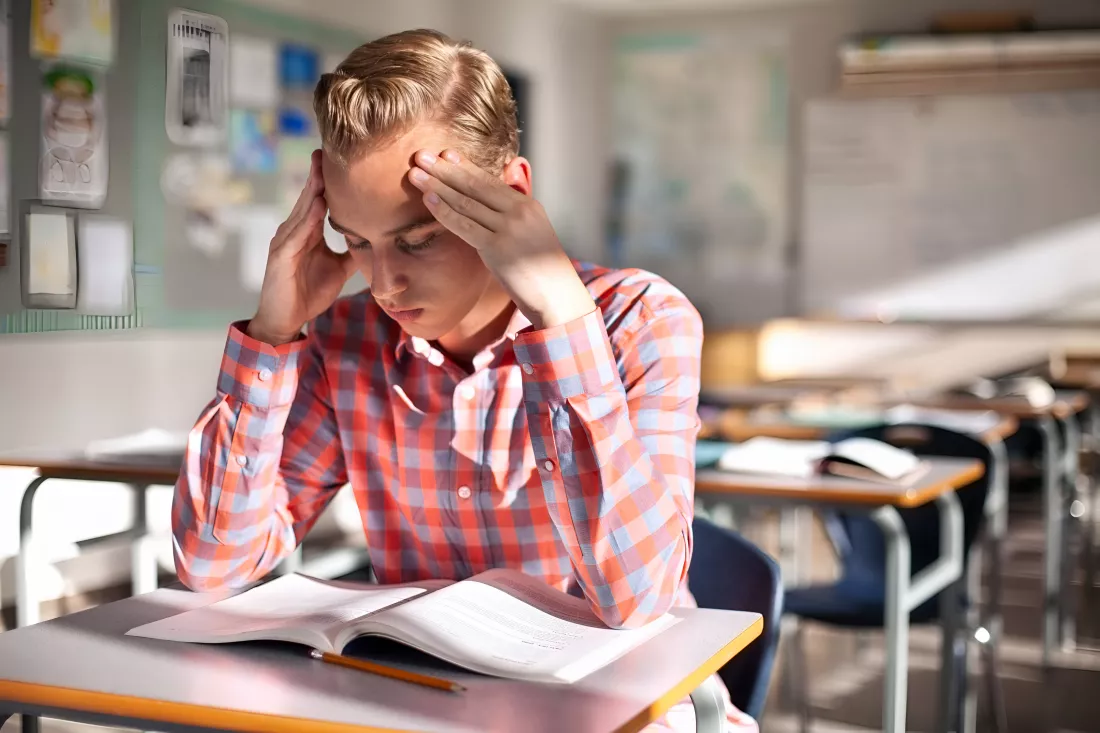 stressed-student-sitting-with-book-desk-male-teenager-is-studying-alone-classroom